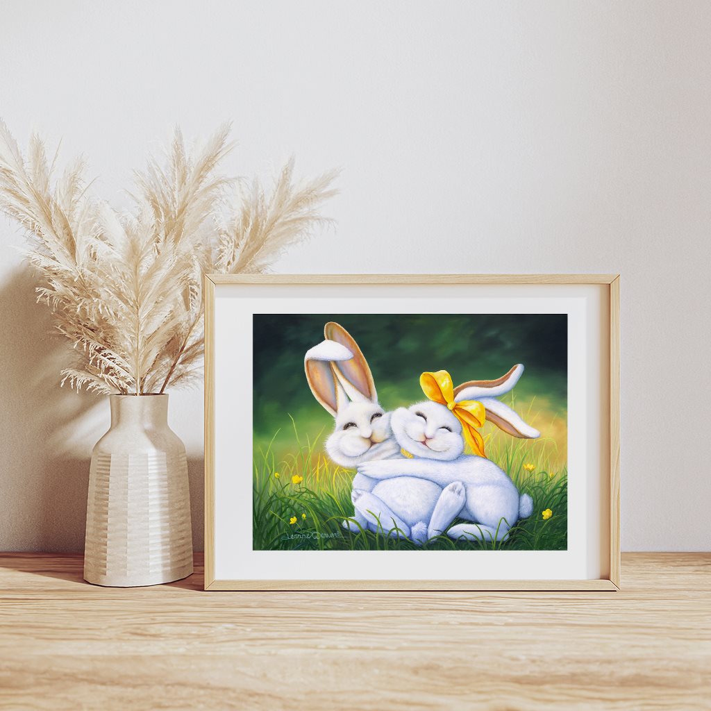 Happy Bunnies giclée paper print in a natural wood frame, resting on a wooden table by artist Jeanne Warren